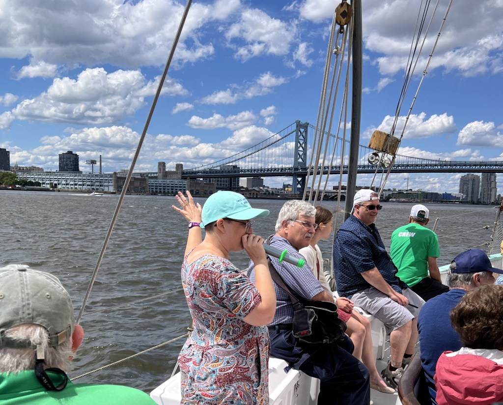 Tour guide speaks to a private tour group sitting on a boat while they gesture towards a suspension bridge